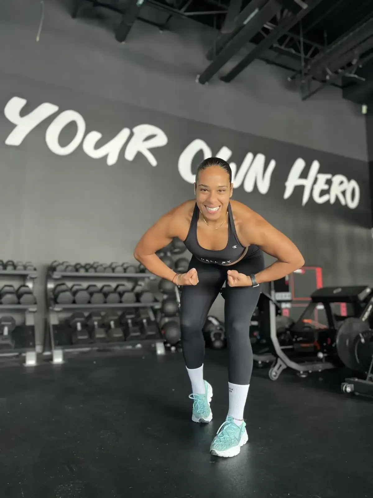 Helga in a squat stance in a gym under a wall that reads Your Own Hero